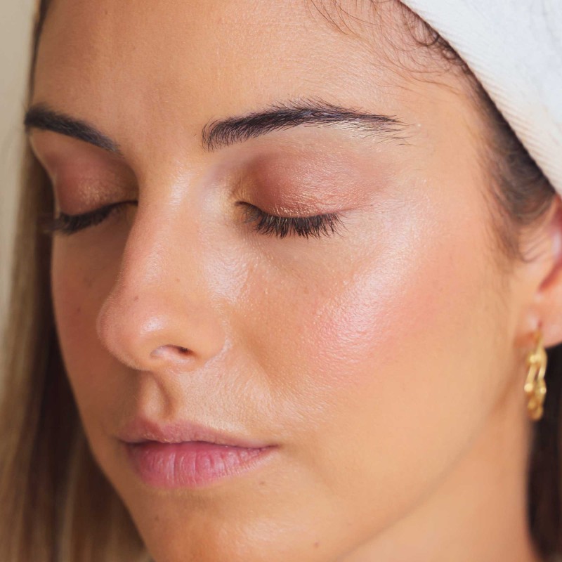 Mujer maquillada con maquillaje natural. Sombras de ojos veganas en tonos tierra y bronce con colorete rosa e iluminador dorado.